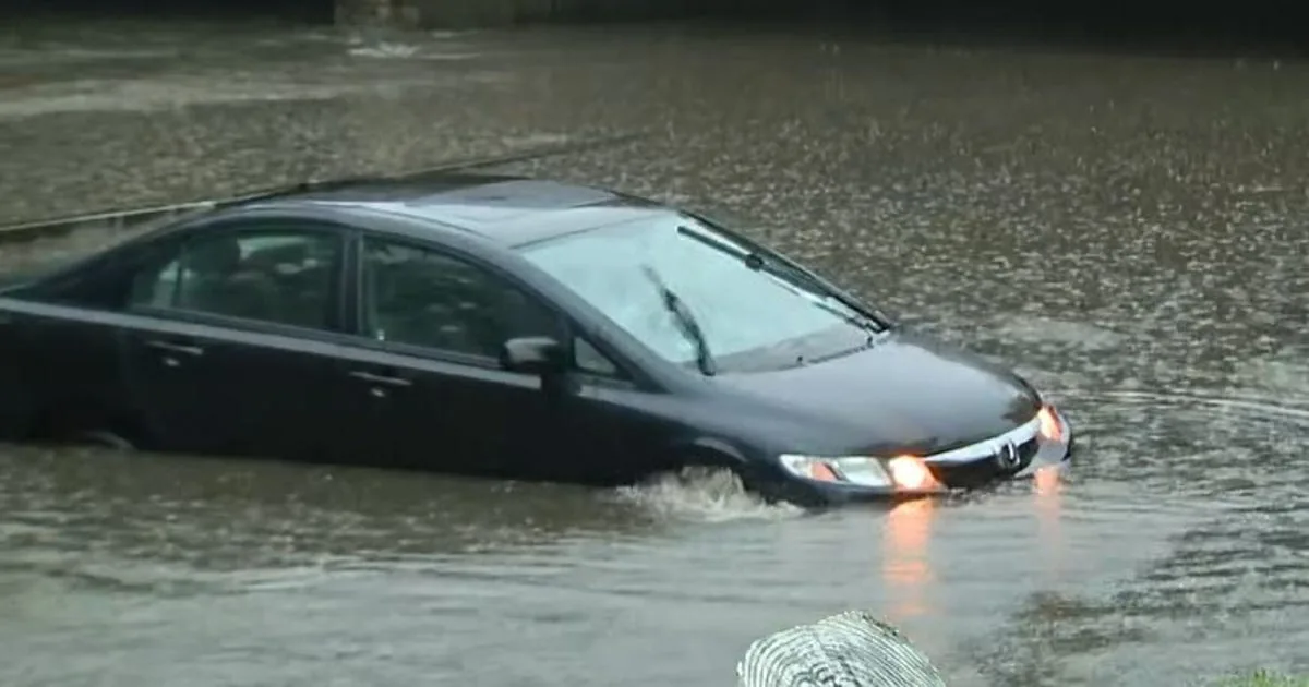Floodwater covers a New York City roadway during heavy rain as drivers navigate a flooded street